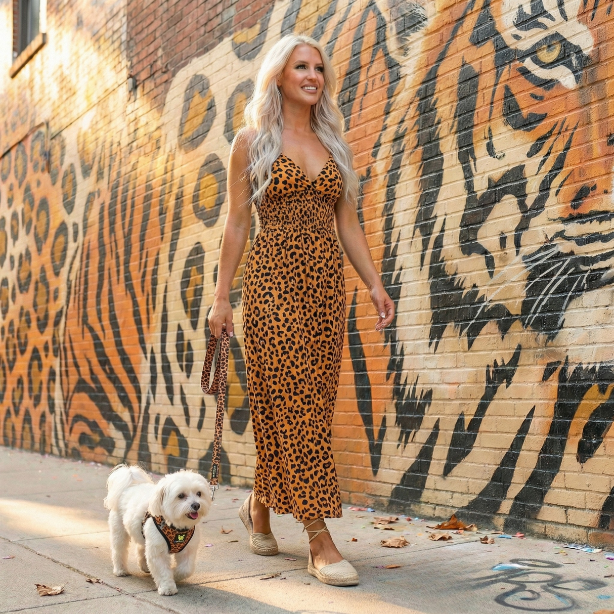 Small white Maltese dog wearing a Cheetah print EcoBark mesh step-in dog harness with reflective strips walking outside with owner by a mural.