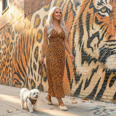 Small white Maltese dog wearing a Cheetah print EcoBark mesh step-in dog harness with reflective strips walking outside with owner by a mural.