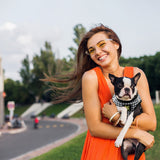 Smiling woman in an orange dress holding a Boston Terrier puppy wearing an EcoBark Houndstooth Step-In Dog Harness.